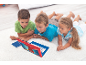 Trois enfants allongés sur le tapis regardent un ordinateur portable de jeu rouge et bleu.