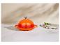 Cocotte en fonte orange avec couvercle, à côté d'un bol de basilic et d'une serviette en lin.