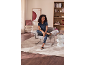 Femme assise dans un fauteuil dans un salon moderne, portant un polo et un pantalon rayé.