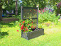 Une jardinière noire avec un treillis et des fleurs rouges dans un jardin.