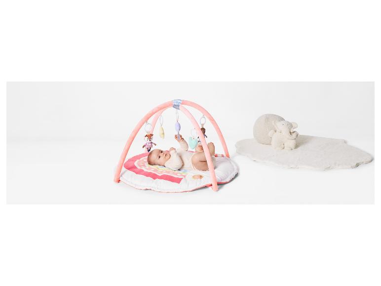Un bébé est allongé sur un tapis de jeu rose avec un arc de jouets et un tapis blanc moelleux avec un éléphant.
