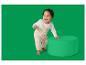 Bébé rieur en salopette tricotée beige et haut blanc, appuyé sur un pouf vert.