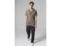 Un homme portant une chemise beige à motif abstrait, un pantalon noir et des baskets blanches.