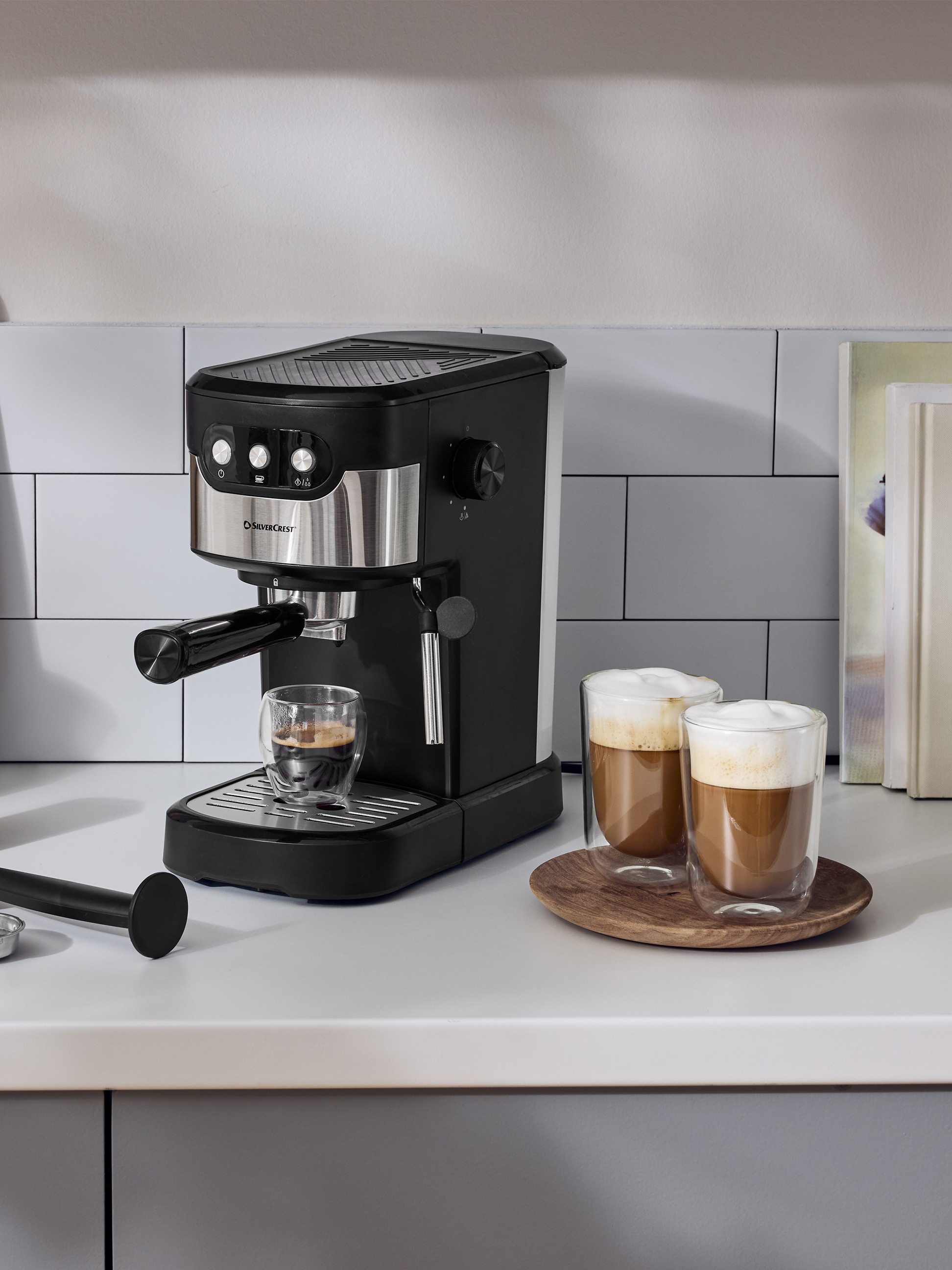 Machine à expresso noire sur un comptoir de cuisine blanc avec deux tasses de café.