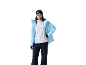 Femme en veste de ski bleu clair, polaire blanche, pantalon de ski bleu foncé, bonnet gris et lunettes de ski.