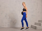 Femme en leggings de sport bleus et chaussures de sport noires tenant un poids.