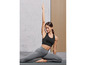 Une femme en top de sport noir et leggings gris fait du yoga sur un tapis.