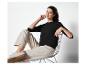 Une femme portant un haut noir et un pantalon beige, assise sur une chaise.