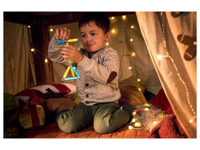 Un garçon joue avec des bâtonnets magnétiques dans une tente décorée de lumières de Noël.