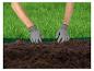 Deux mains en gants de jardinage travaillent la terre le long d'une bordure d'herbe verte.