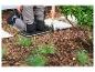 Personne agenouillée sur un coussin de jardinage, utilisant une petite pelle pour jardiner.