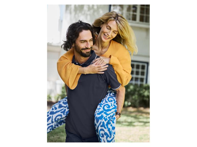 Couple heureux, elle porte une robe orange et un pantalon bleu à motifs, lui un polo noir.