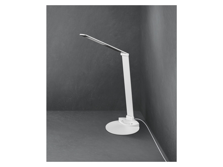 Une lampe de bureau blanche avec un bras flexible dans un coin sur un sol gris.