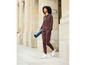 Une femme en sweat-shirt et pantalon de survêtement marrons marche avec un tapis de yoga.