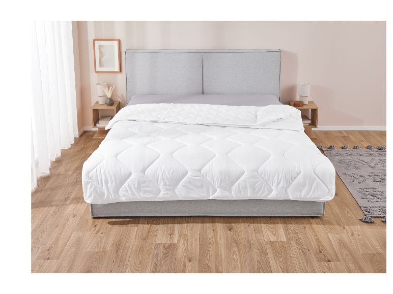 Une couette blanche à motif matelassé sur un lit gris moderne.