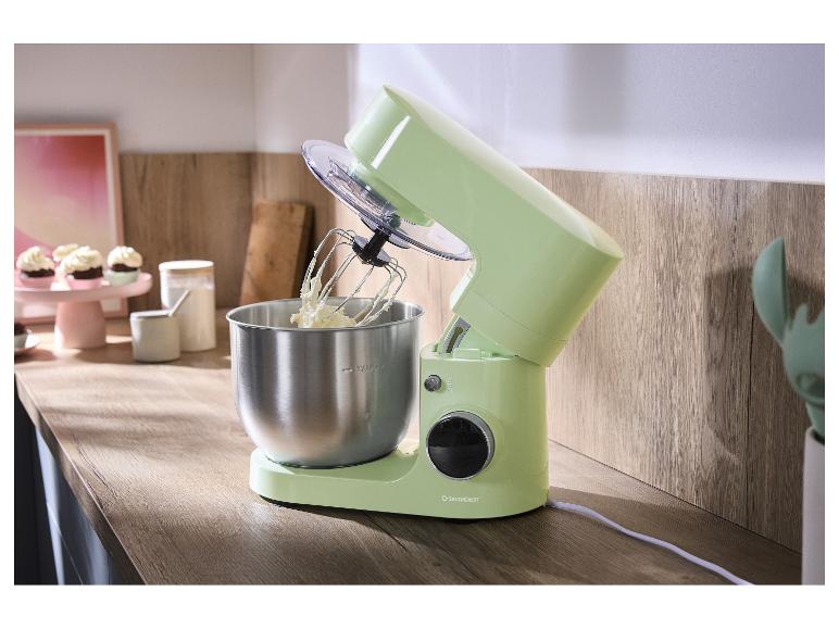 Robot pâtissier vert clair avec bol en métal et fouet, sur un comptoir de cuisine en bois.