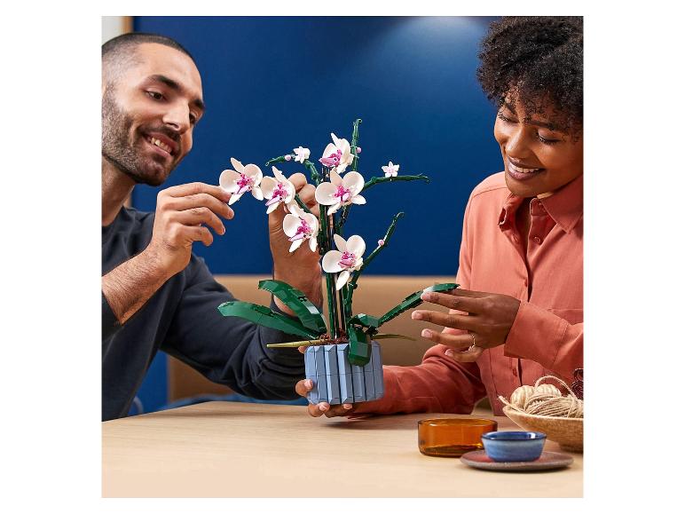 Deux personnes assemblent une orchidée LEGO, posée sur une table en bois.