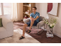 Homme en short et sandales, assis dans un fauteuil dans un salon moderne.