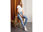 Une femme portant un t-shirt blanc, un jean skinny bleu et des baskets blanches.