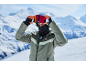 Skieur avec casque, lunettes et cagoule, portant une veste verte, à la montagne.