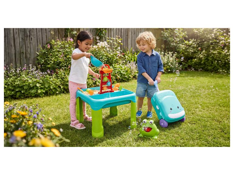 Deux enfants jouent avec une table d'eau et de sable et une machine à bulles dans le jardin.
