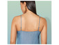 Une femme porte une robe en jean bleu avec des bretelles fines.