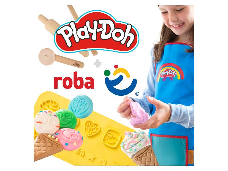 Fille souriante en tablier bleu pétrissant de la pâte à modeler rose, avec des outils en bois et des moules en silicone.