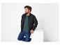 Un homme portant une veste noire, un t-shirt vert foncé et un jean bleu.
