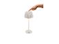 Lampe de table blanche avec abat-jour plissé, allumée par un doigt.