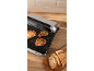 Gril de contact électrique avec de la viande grillée et du pain sur un plan de travail en bois.
