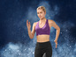 Une femme en brassière de sport violet et leggings noirs court devant un fond bleu.