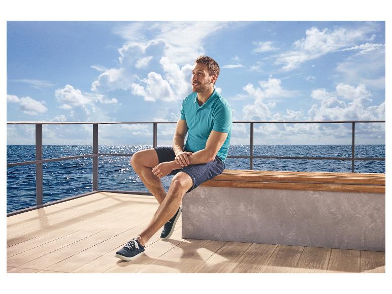 Homme en polo bleu et short, portant des chaussures de loisirs ESMARA MEN, assis au bord de la mer.
