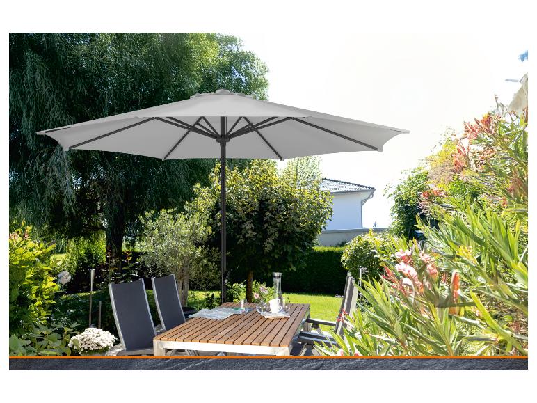 Parasol gris et table de jardin en bois avec chaises dans un jardin verdoyant.