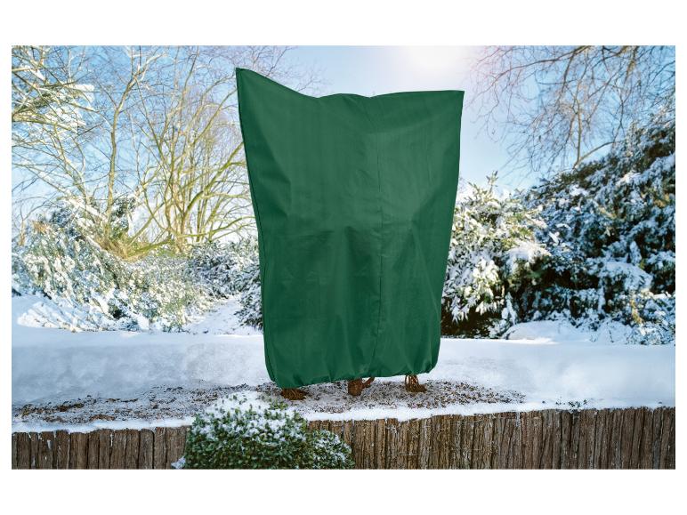 Plante recouverte d'une bâche verte dans un paysage hivernal enneigé.