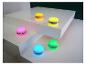 Cinq petits haut-parleurs ronds et colorés sur des surfaces blanches avec un fond vert foncé.