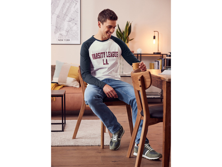 Un homme portant un t-shirt blanc, un jean bleu et des baskets vertes.
