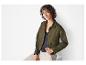 Une femme porte une veste verte, un top noir et un pantalon beige.