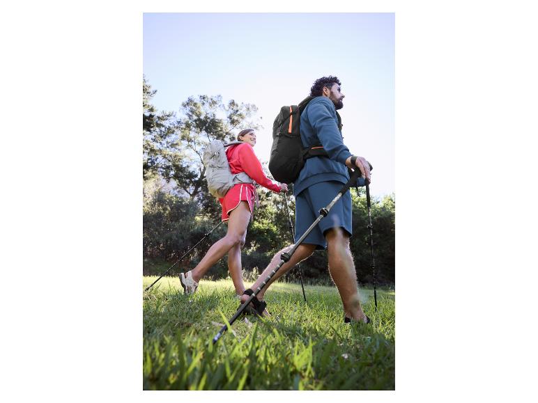 Couple en randonnée avec sacs à dos et bâtons de marche sur terrain herbeux.