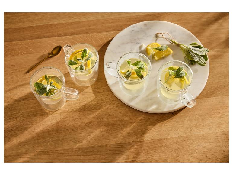 Quatre verres de boisson au citron et à la sauge sur une table en bois avec un plateau en marbre.