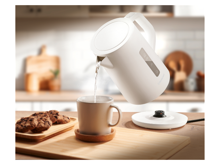 Une bouilloire électrique SilverCrest blanche verse de l'eau dans une tasse sur une table en bois.