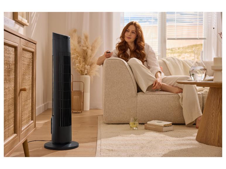 Femme se relaxant sur un canapé avec un ventilateur tour, une télécommande et une boisson.