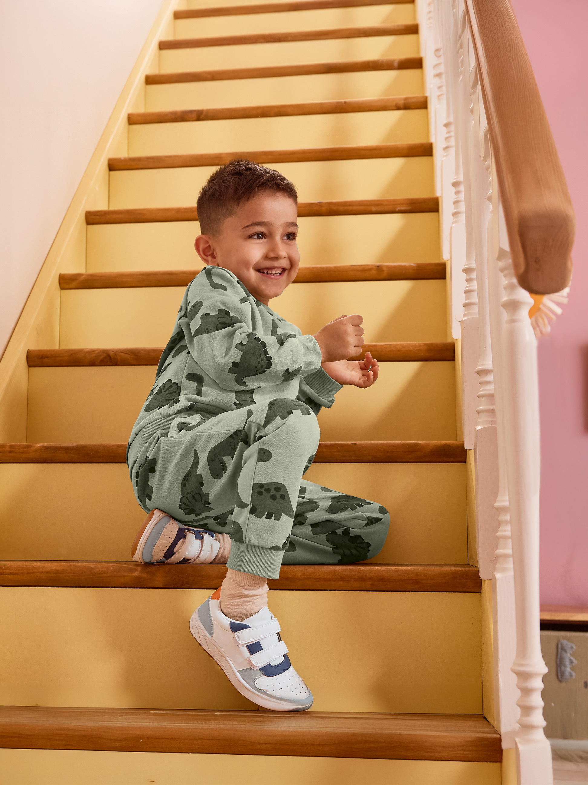 Garçon en pyjama dinosaure vert assis sur les escaliers, souriant.