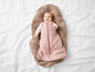 Un bébé dans une gigoteuse rose à imprimé, allongé sur une couverture beige.