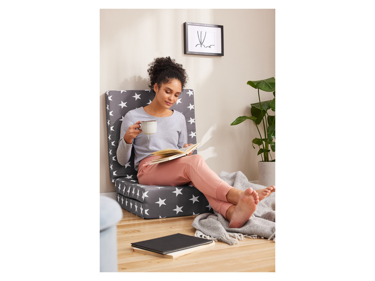 Une femme assise sur un matelas pliable à étoiles, lisant un livre.