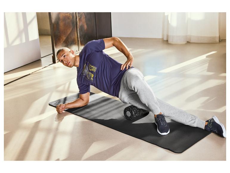 Un homme utilise un rouleau en mousse pour faire de l'exercice sur un tapis de yoga.