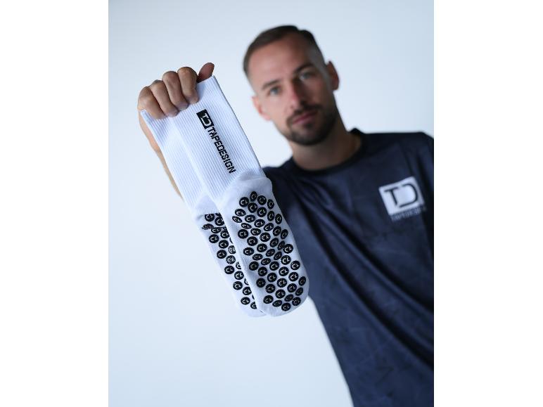 Homme tenant des chaussettes de sport blanches TAPEDESIGN avec picots antidérapants.