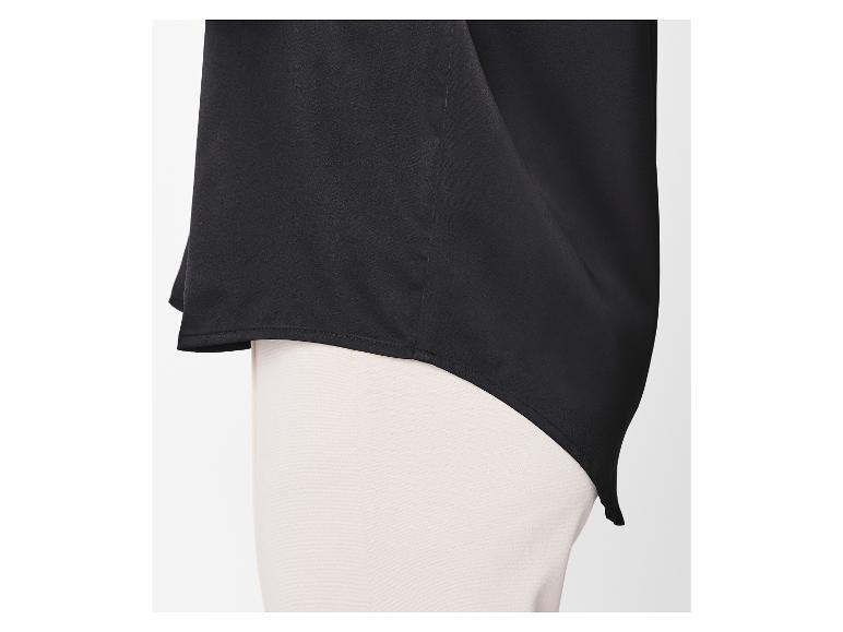 Chemisier noir à ourlet asymétrique sur un pantalon clair.