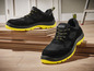 Chaussures de sécurité Parkside noires à semelle jaune sur une pile de bois