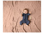 Un bébé dans une grenouillère rayée est allongé sur une couverture rose.