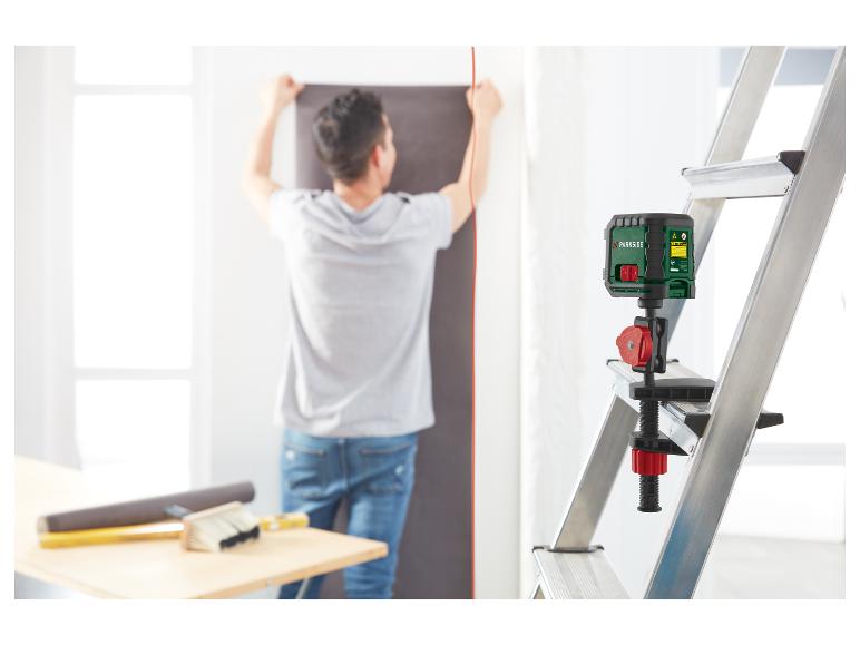 Homme utilisant un niveau laser Parkside monté sur une échelle pour poser du papier peint.